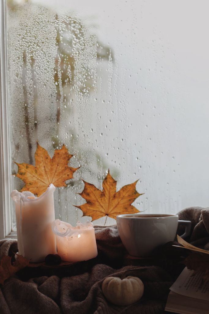 Warm autumn atmosphere with lit candles and cup of coffee by a rainy window.
