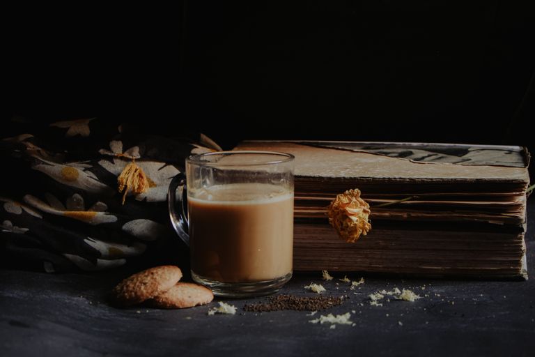 Dark atmospheric still life of a cozy tea setup with cookies and vintage books.